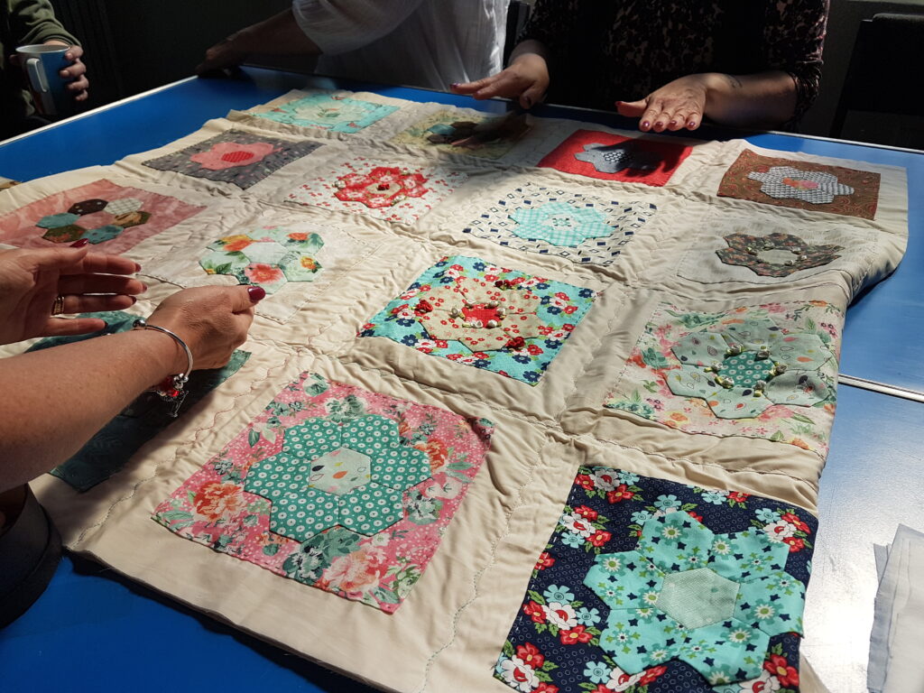 A cozy floral quilt with two sets of hands working on it.