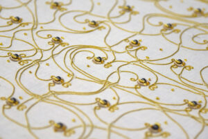 Closeup of white fabric with intricately entangled golden embroidery with small magnets in it.